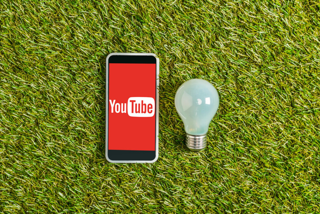Smartphone avec logo YouTube et ampoule sur l'herbe.