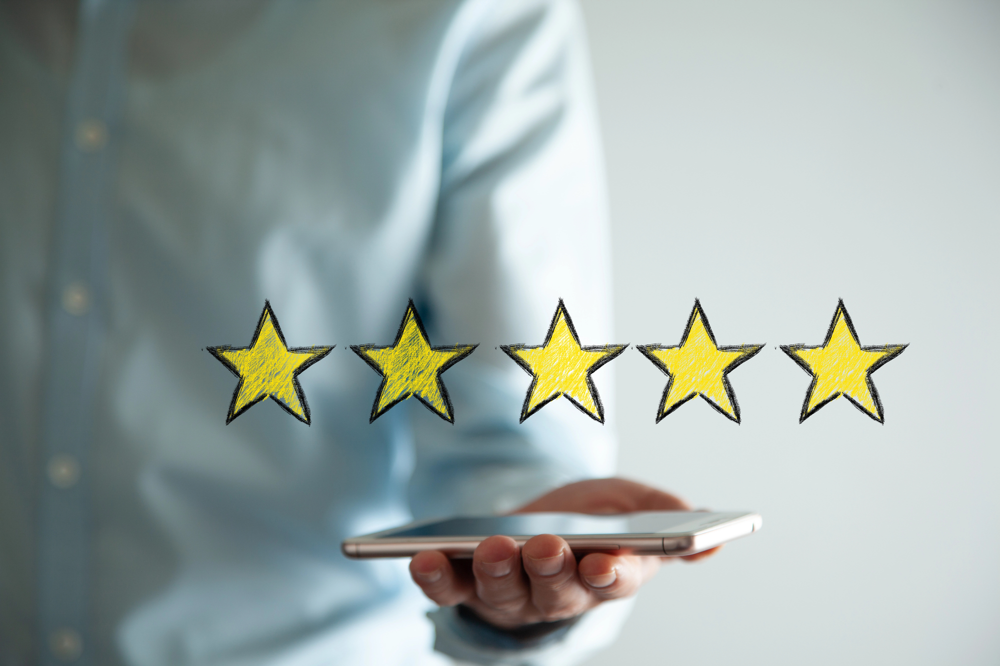 Main tenant un smartphone surmonté de cinq étoiles jaunes