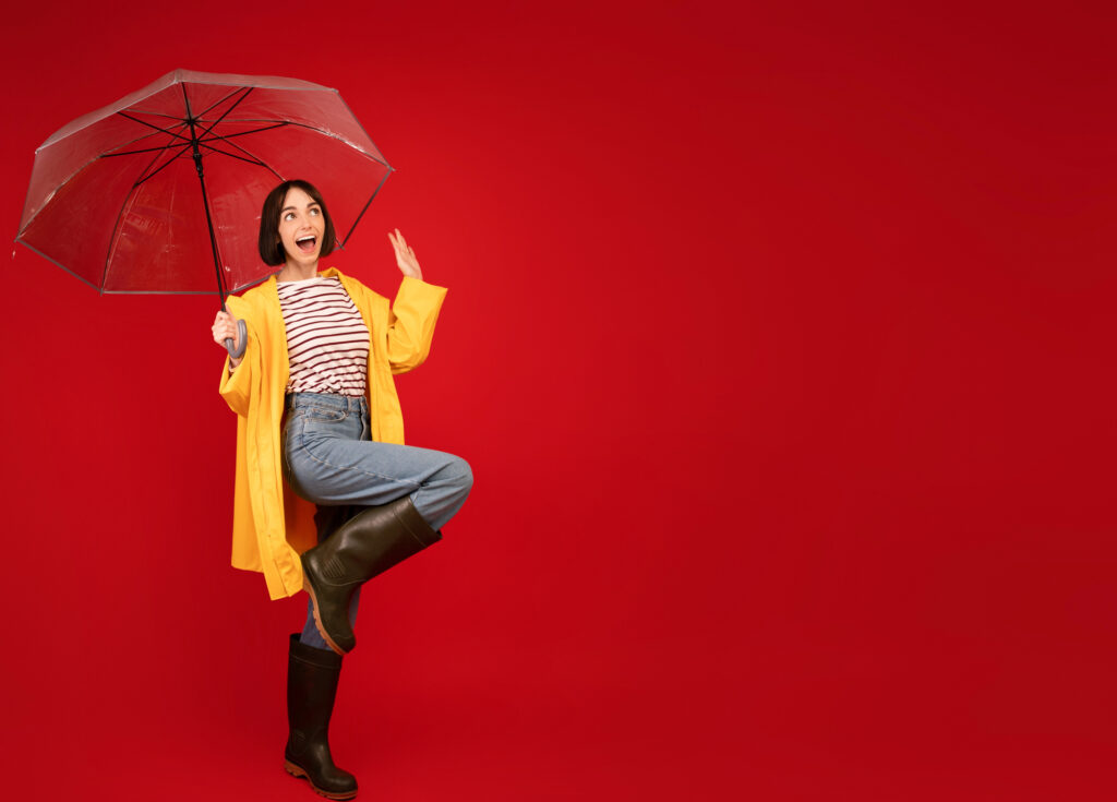 Femme en imperméable jaune avec parapluie sur fond rouge.