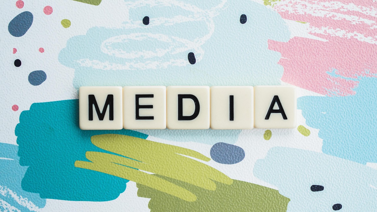 Lettres de jeu scrabble formant le mot "MEDIA" sur fond coloré.