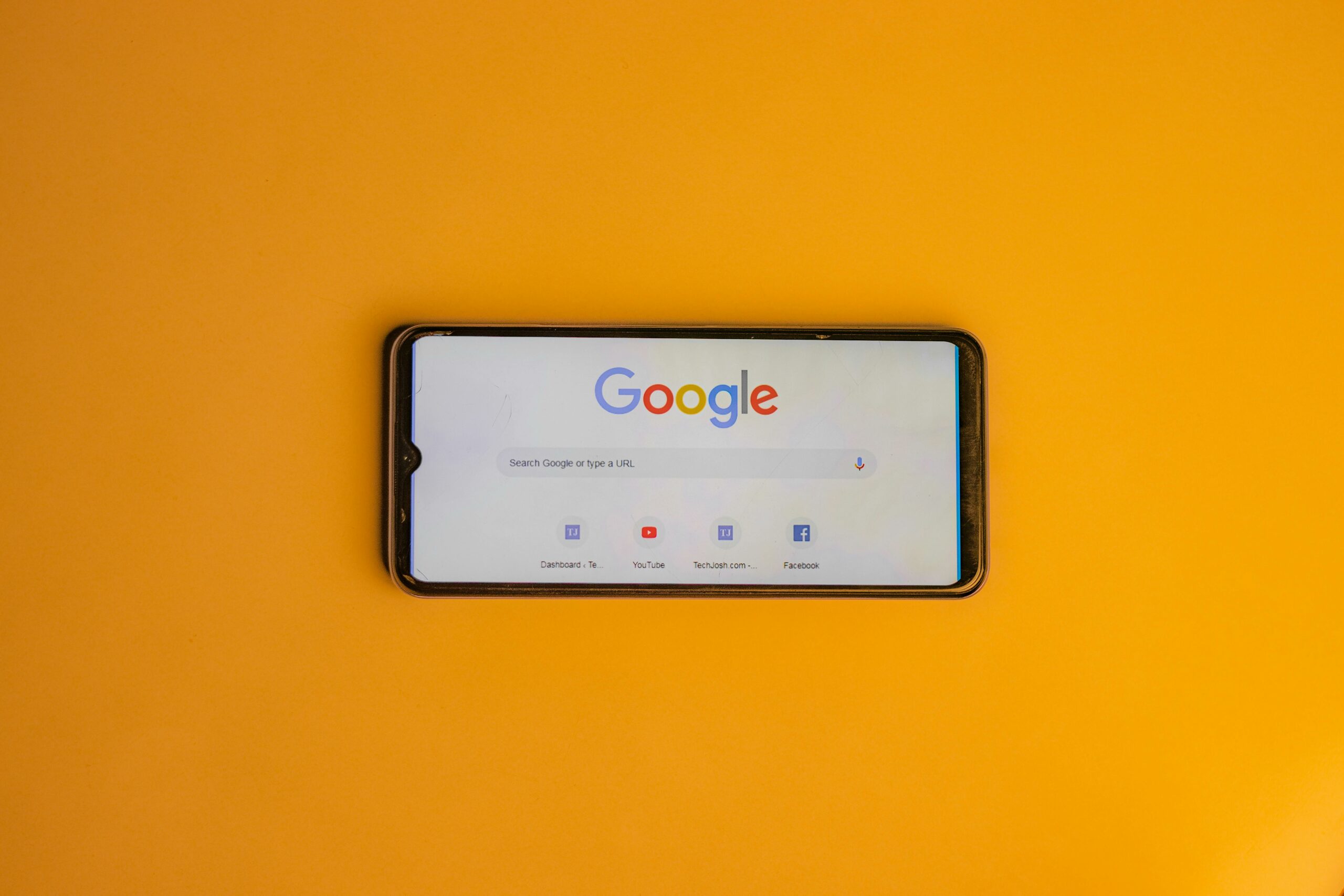 Smartphone affichant le moteur de recherche Google sur fond orange.