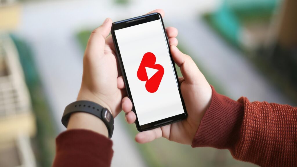 Mains tenant un smartphone affichant le logo YouTube Shorts