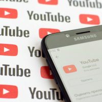 Smartphone affichant l'application YouTube sur un fond de logos