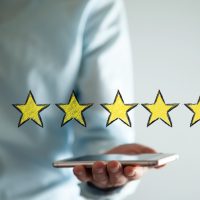 Main tenant un smartphone surmonté de cinq étoiles jaunes