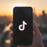 Main tenant un smartphone affichant l'application TikTok au coucher du soleil
